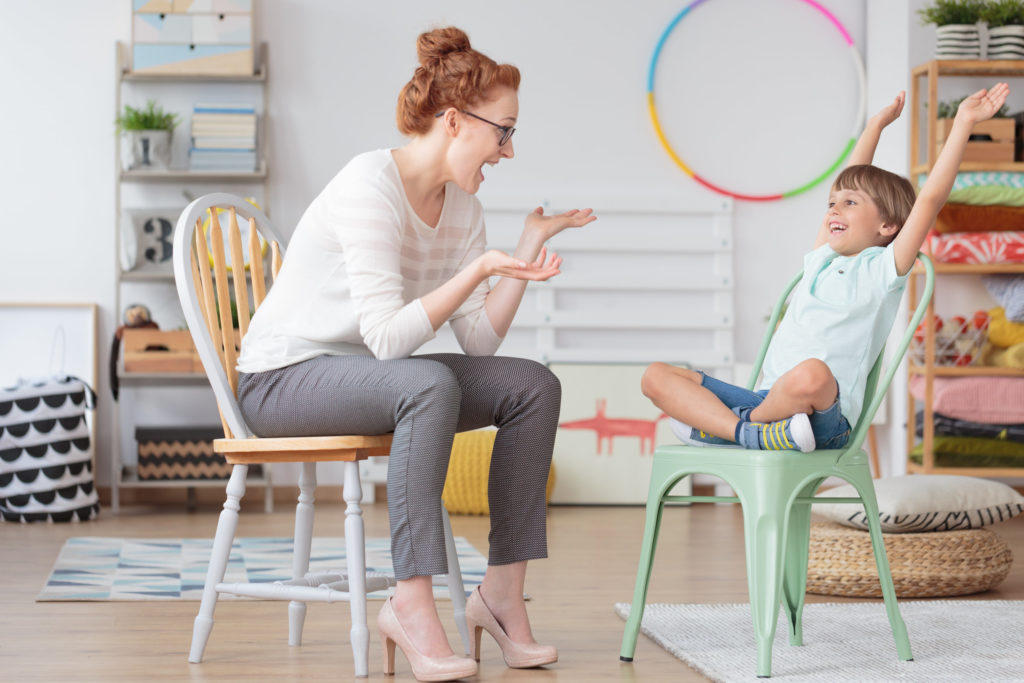 Child psychologist and young kid with ADHD during therapy session in primary school interior